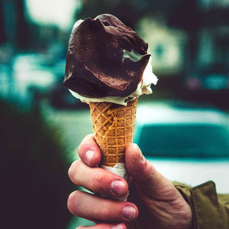 A hand holding an ice cream cone with a chocolate scoop